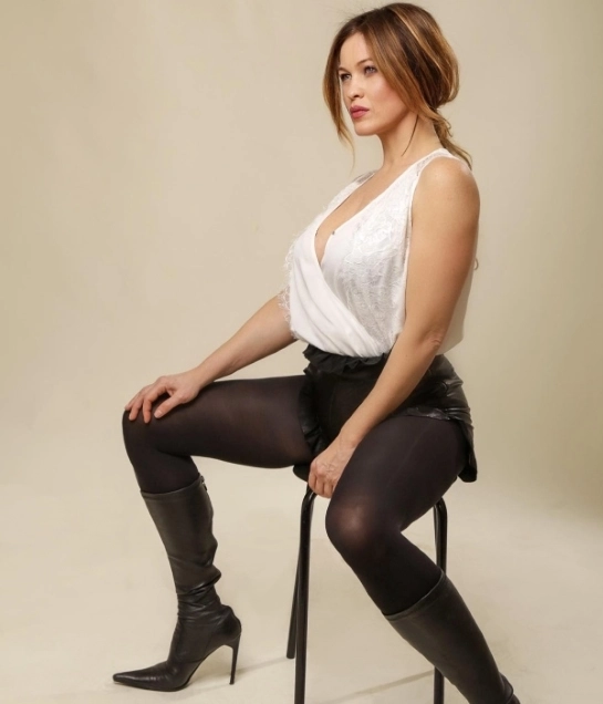 Yulia Mayarchuk in a white sweater, black tights and black shorts sits on a chair, professional photo
